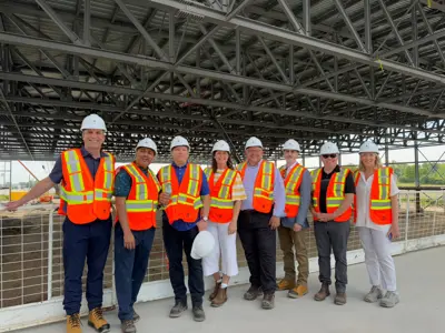 Group of adults in construction clothes standing in front of recreation centre being built