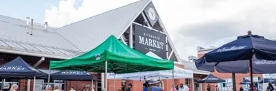 vendor tables in front of the kitchener market building with people walking around