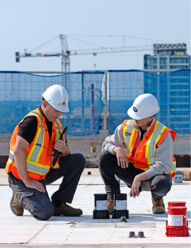 Two City of Kitchener staff members are kneeling on a flat rooftop looking at installed technology