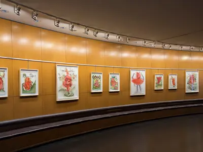 Artwork with red figures on light coloured backgrounds hanging from the wall of the Rotunda Gallery