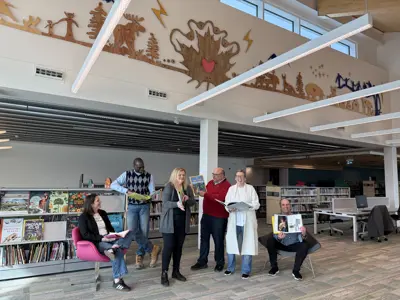 Group of adults standing in library in front of rack of books