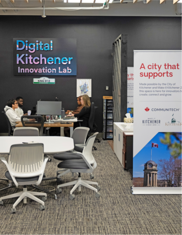 Four people sitting at a meeting table in a room with a Digital Kitchener logo on the wall